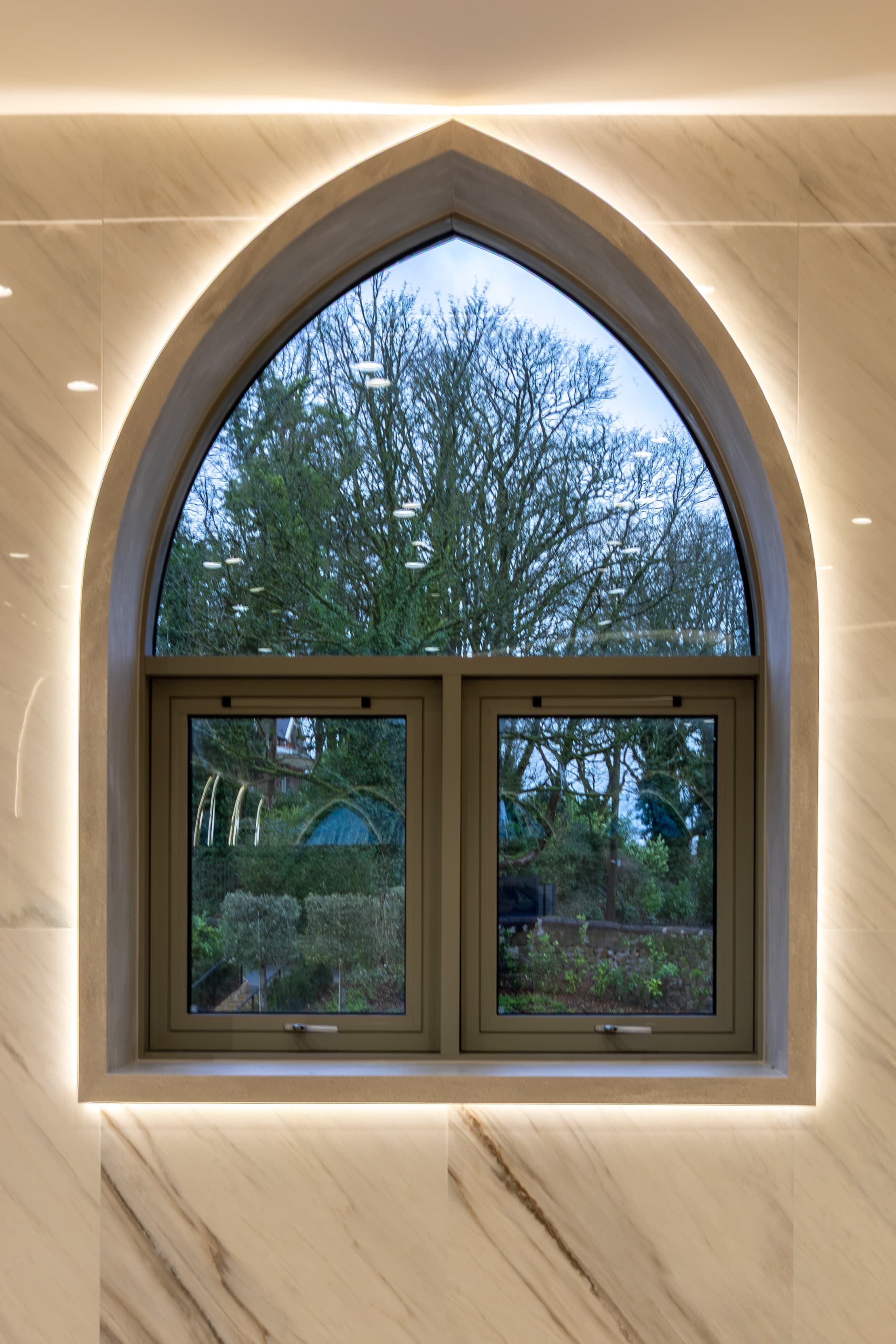 A tall arched window in the masjid, looking out onto trees