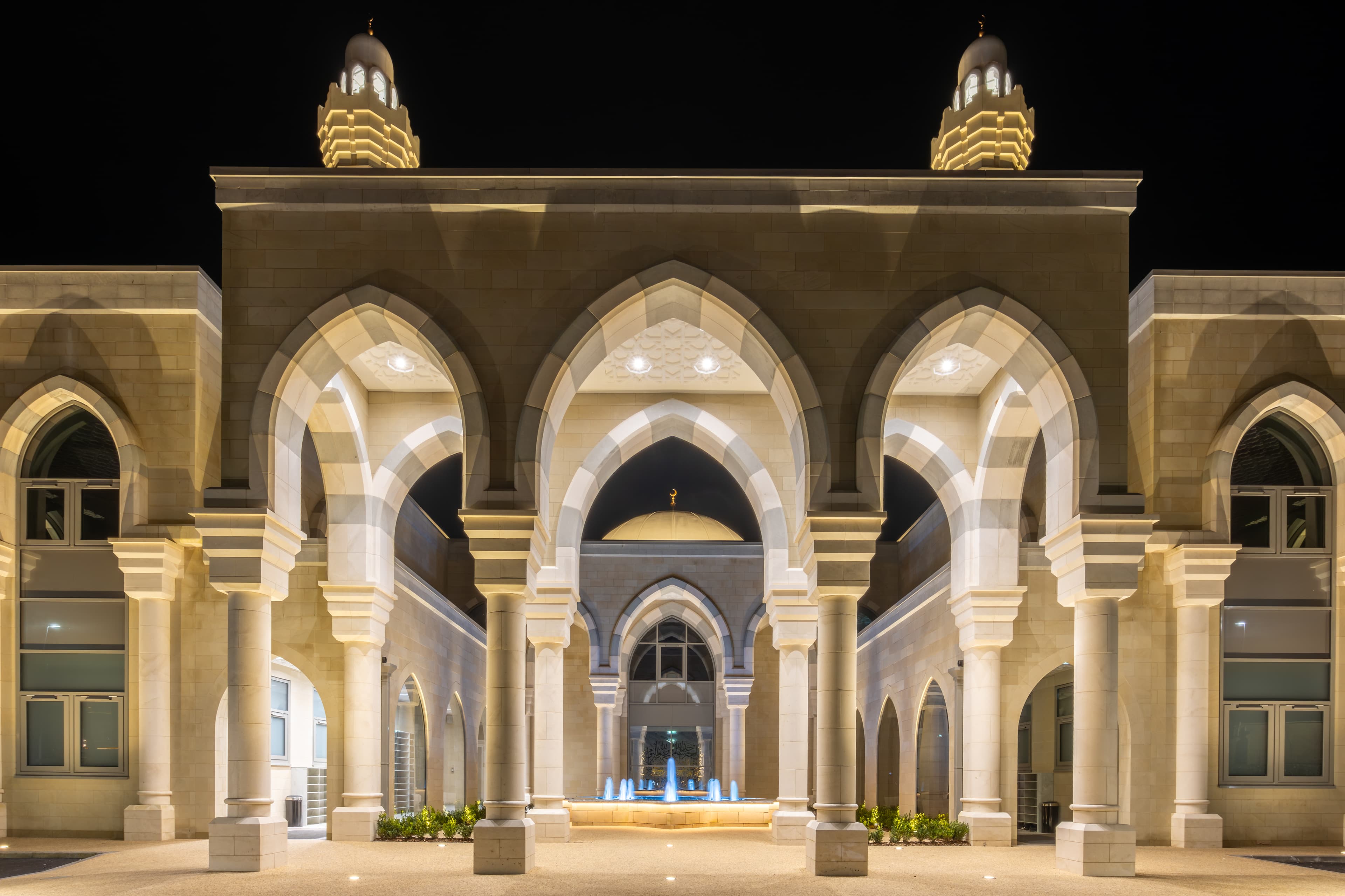 The front of the mosque at night: a broad arched entrance bay flanked by two small domes, lit against a dark sky.