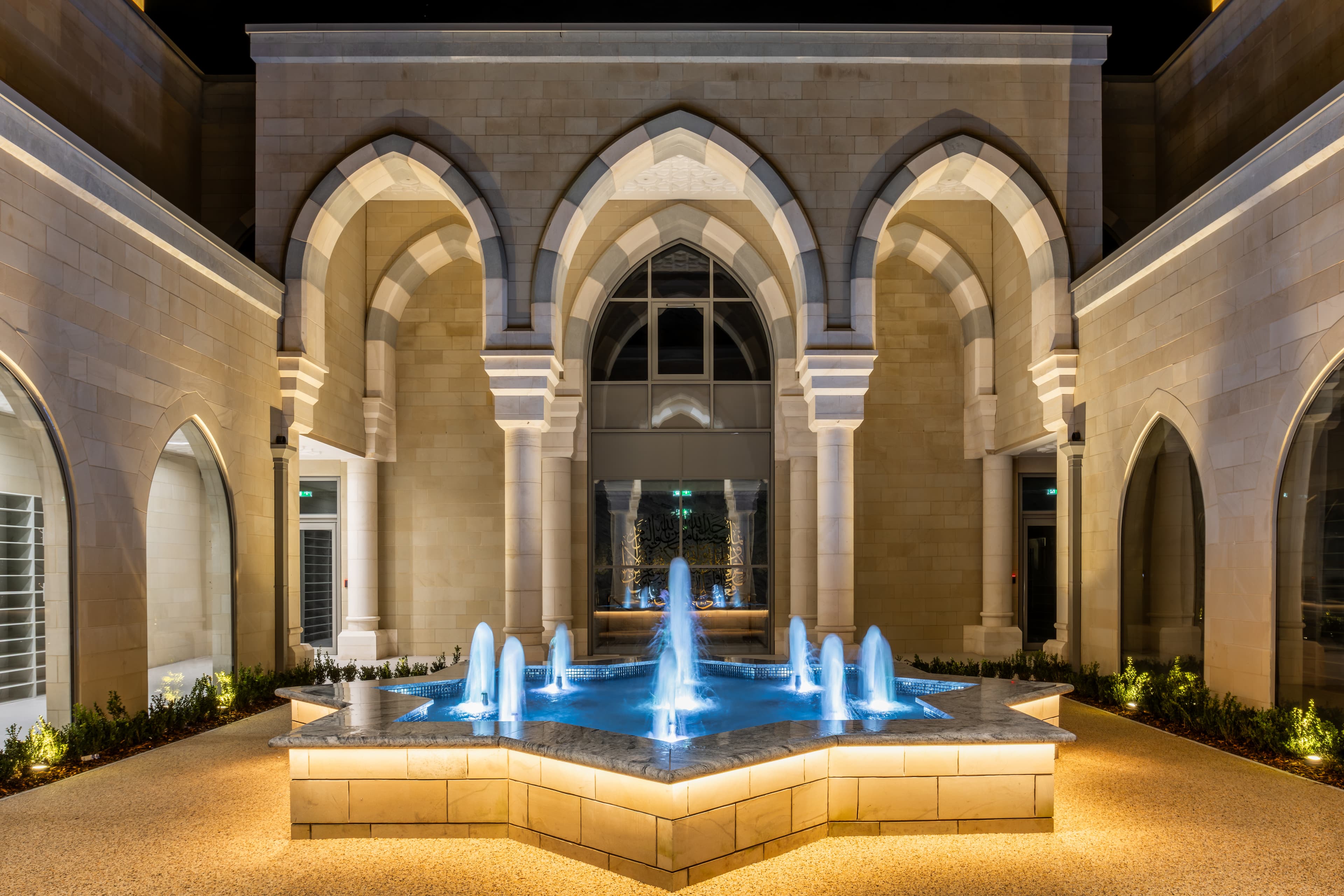 The courtyard at night: a colonnade of pointed arches around the blue-lit star fountain.