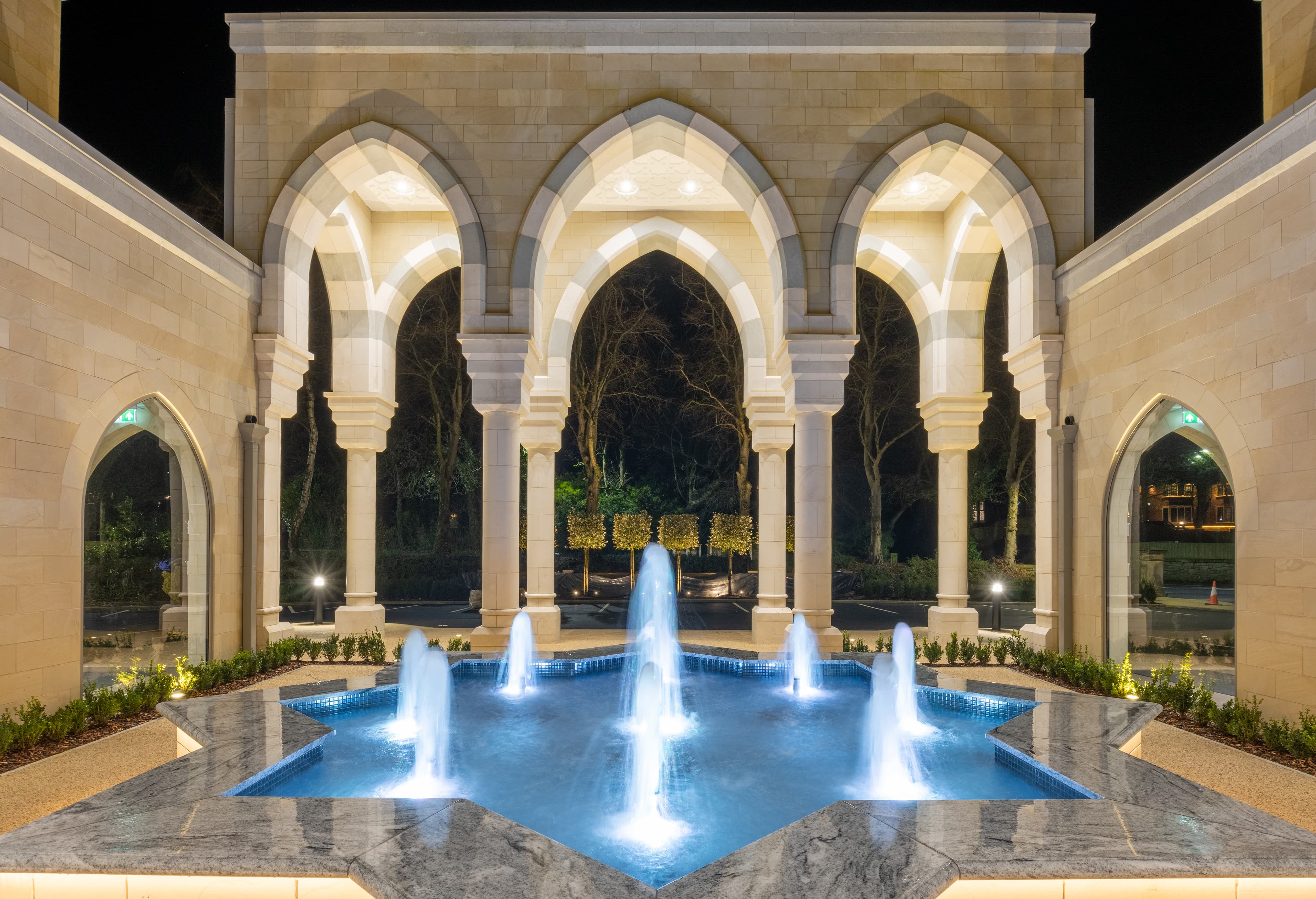 A symmetrical view of the courtyard arcade at night, the lit fountain sitting exactly on the central axis.