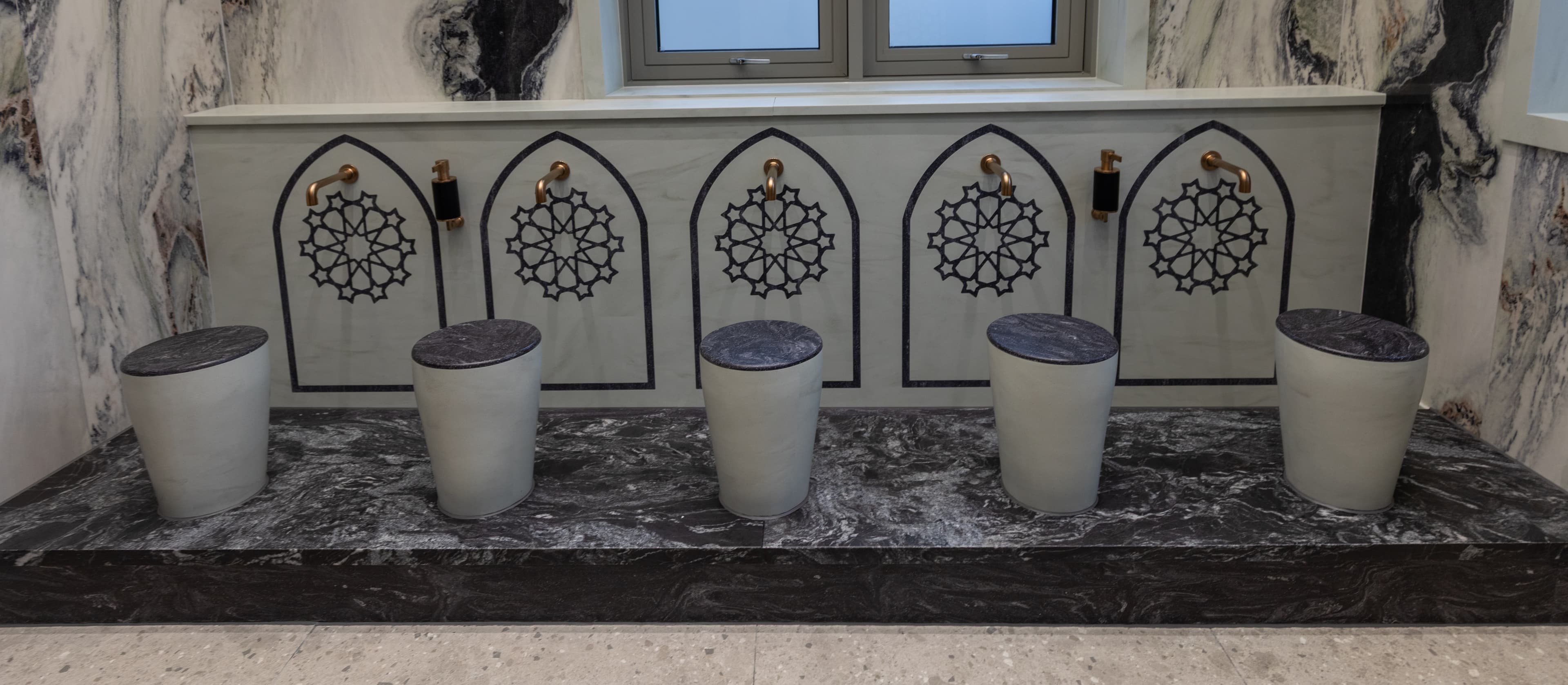 The wuḍhū area: a long dark marble bench beneath a row of carved arched geometric motifs, with stone stools below.