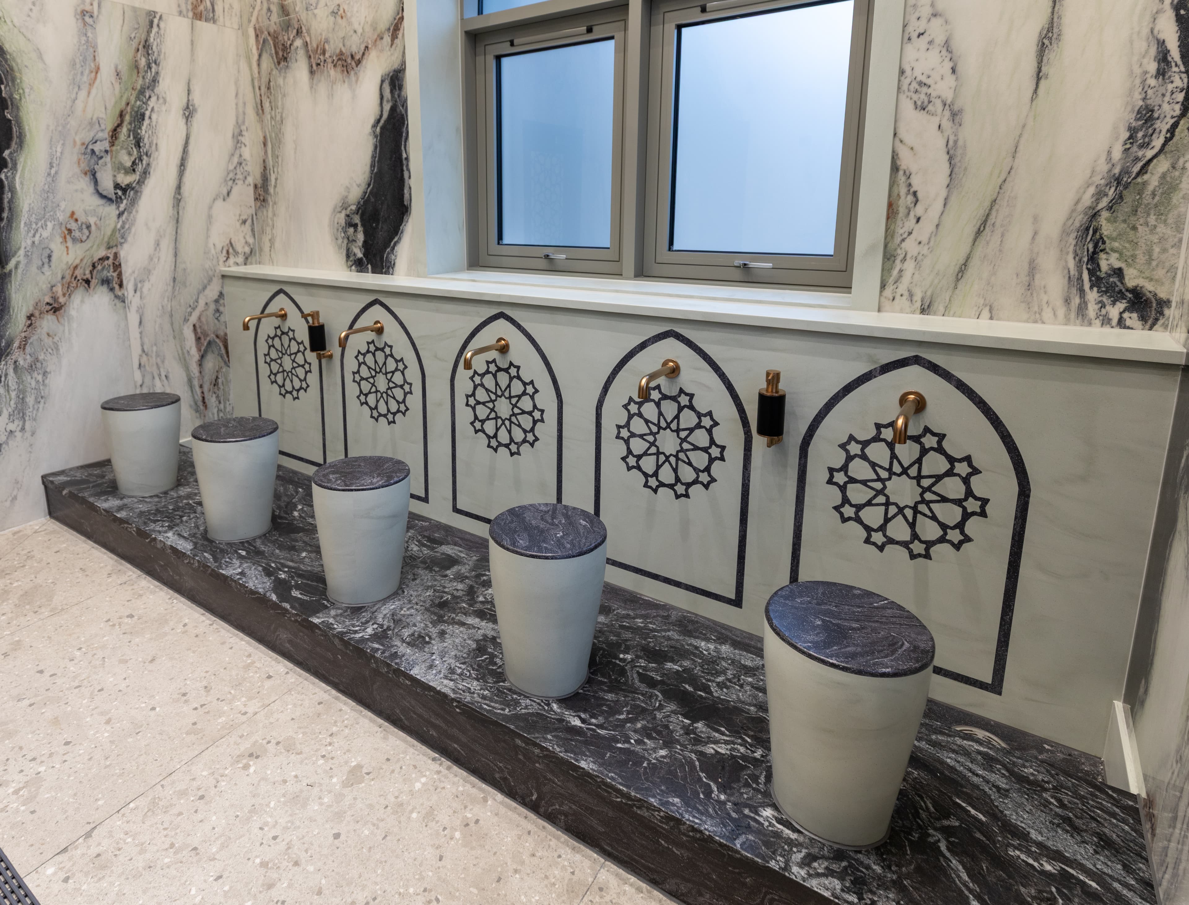 Wuḍūʾ stations with brass taps beneath carved arches